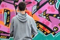 A young graffiti artist in a gray hoodie looks at the wall with