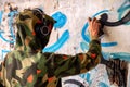 Young graffiti artist in hoodie spraying the wall