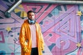 Young graffiti painter standing near the wall with his paintings with copy space