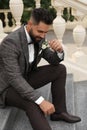 Young groom in elegant suit with beautiful boutonniere sitting on stairs outdoors