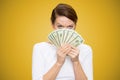 Grumpy woman covering face with heap of bills looking at camera on yellow background