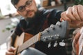 Young guitarist hipster at home with guitar fixing tuning pegs close-up