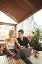 Young guy and attractive girl sitting on terrace in restaurant with laptop computer on table, drinking coffee, using computer and