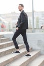 A young guy with a beard and in a suit rises up the stairs in the street. Outside.