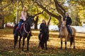 A guy, a girl and a little girl ride on black horses and ponies in an autumn park.