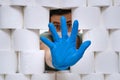 Young guy behind the wall of toilet paper shows stop hand gesture