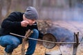 A young guy tastes the broth being cooked over a campfire