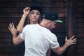 A guy in a white t-shirt shields a girl in a baseball cap against a wall Royalty Free Stock Photo