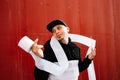 A young guy in black sports clothes and a baseball cap on the street, standing near a red wall wrapped in toilet paper ribbons