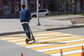 A young guy in a blue bomber jacket and jeans on an electric scooter moves very quickly along a pedestrian crossing, leaning to Royalty Free Stock Photo