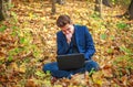 Young guy businessman in classic blue jacket with laptop sitting in forest park in autumn