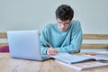 Young guy college student sitting at desk in classroom, using laptop, writing in notebook Royalty Free Stock Photo