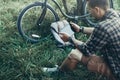 Young Guy Cyclist Sits On Summer Meadow Near Bicycle, Holding And Looking At Tablet Recreation Resting Travel Destination Concept Royalty Free Stock Photo