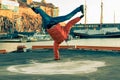 Young guy dancing break dance on the waterfront in an orange jacket in winter. Royalty Free Stock Photo