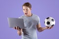 Young guy disappointed at his soccer team defeat, watching football game on laptop computer, lilac studio background Royalty Free Stock Photo