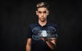 Young guy dressed in a black t-shirt holds a quadcopter and looking at a camera. Isolated on a dark background.