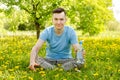 Young guy dressed in a blue t-shirt, drinks water from a bottle, sits on a green grass and yellow dandelion background Royalty Free Stock Photo