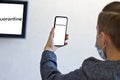 Young guy in face mask holding mobile phone with quarantine inscription on screen