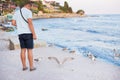 A young guy is feeding a flock of seagulls. Sun, summer, sea