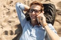 Young guy with glasses, lying on the beach on the sand, and talking on the phone, work on vacation, suitable for advertising Royalty Free Stock Photo