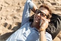 Young guy with glasses, lying on the beach on the sand, and talking on the phone, work on vacation, suitable for advertising Royalty Free Stock Photo