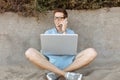 Young guy with glasses, working on his laptop and talking on the phone on the beach, working on vacation, suitable for advertising Royalty Free Stock Photo