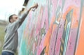 A young guy in a gray hoodie paints graffiti in pink and green c