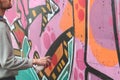 A young guy in a gray hoodie paints graffiti in pink and green c