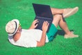 Modern man lying in grass and using laptop