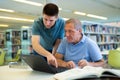 Young guy helping older man in laptop interface in library Royalty Free Stock Photo