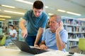 Young guy helping older man in laptop interface in library Royalty Free Stock Photo
