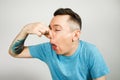 Young guy inserts two fingers in the mouth to induce vomiting, on a light background