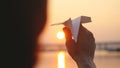 Young guy launch paper plane against the sea during sunset with sun flare and reflections in the water, as in childhood Royalty Free Stock Photo