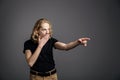 A young guy with long blonde hair pokes his index finger to the side in surprise. A young man is showing something on a gray Royalty Free Stock Photo