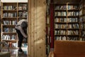 Young guy looking for books in the library with wooden bookcases. Knowledge and education. Blurred Royalty Free Stock Photo