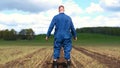 A young guy man, a farmer in a working uniform, walks across a field in rubber boots. Concept of: Freedom, Rubber boots, Lifesty