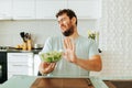 Young man take care of health is on diet grimaces with displeasure and pushes away a bowl of salad. Royalty Free Stock Photo