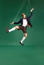 Young guy, marionette on string in motion against green studio background. Puppet. Pressure and manipulation