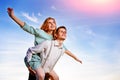 Young guy piggybacking cheerful girlfriend like airplane on the background of sky