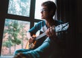 Young guy plaing on guitar and sits near the window Royalty Free Stock Photo