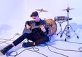 Young guy playing acoustic guitar sitting on the floor leaning on a drum barrel Royalty Free Stock Photo