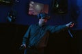 Young guy plays video games in virtual reality headset in dark game room. High tech innovative gaming club