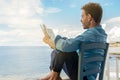 Young guy reading book at sea enjoying summer vacations on beautiful beach feeling free Royalty Free Stock Photo