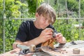 Young guy repairs the wheels on a skateboard on a wooden stall in the garden