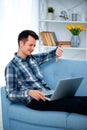 Young guy showing thumb down with his hand at his laptop computer. Man sitting at home on cozy blue sofa at home, wearing casual Royalty Free Stock Photo