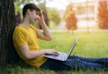 A young guy sits and smiles on the lawn and communicates with friends via video communication using a laptop Royalty Free Stock Photo