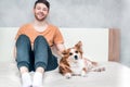 Young guy is sitting on the bed with his ginger dog. Close-up portrait. Owner and dog