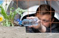 A young guy sitting in prison watering from a plastic bottle dandelion flower growing behind a rusty lattice on the loose. The