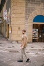 A young guy with a straw hat, a white unbuttoned shirt and a sand jacket, a small beard walks around the city of