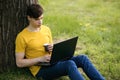 A young guy student sits on the lawn and drinks coffee, holding a laptop in his hands Royalty Free Stock Photo